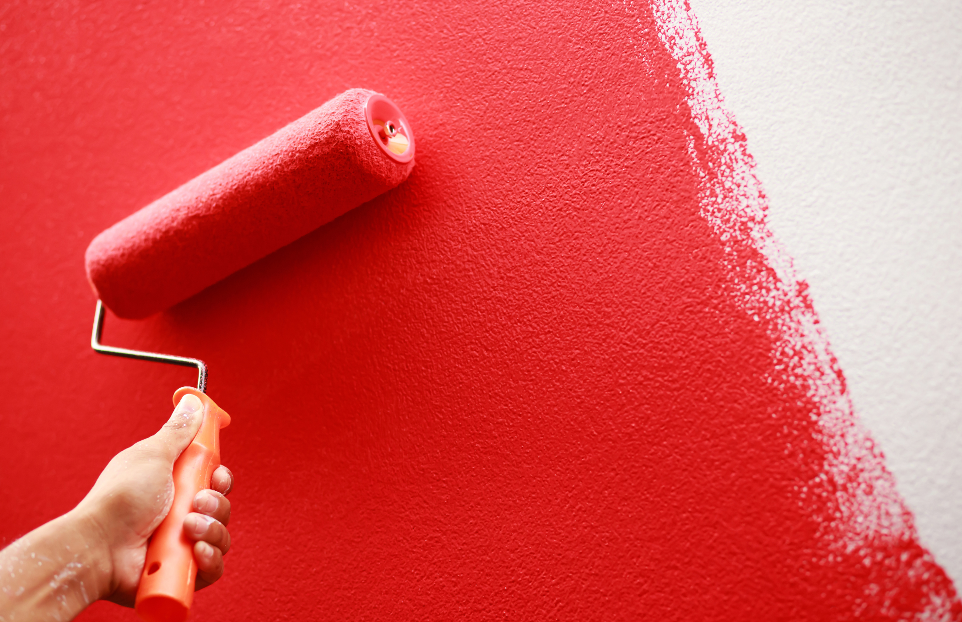 Person painting the wall red using a paint roller 
