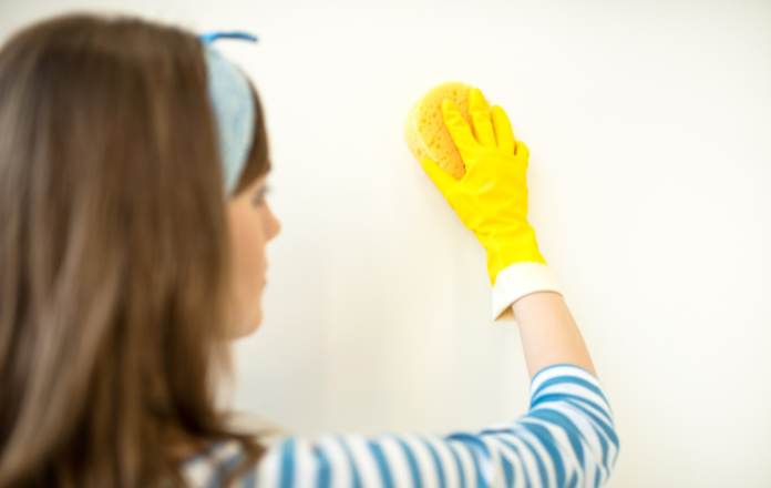 Woman in blue striped shirt cleaning wall with sponge
