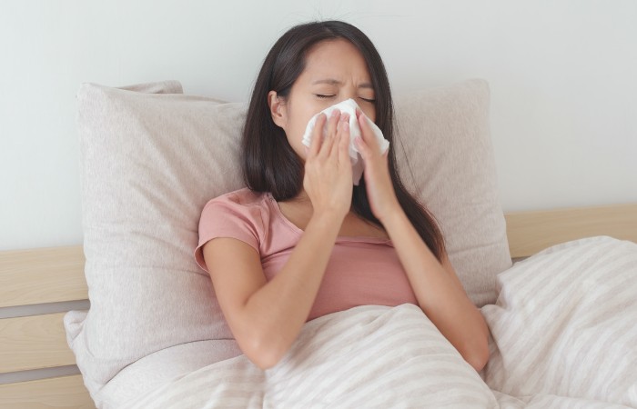 lady-sitting-on-the-bed-sneezing-on-a-handkerchief